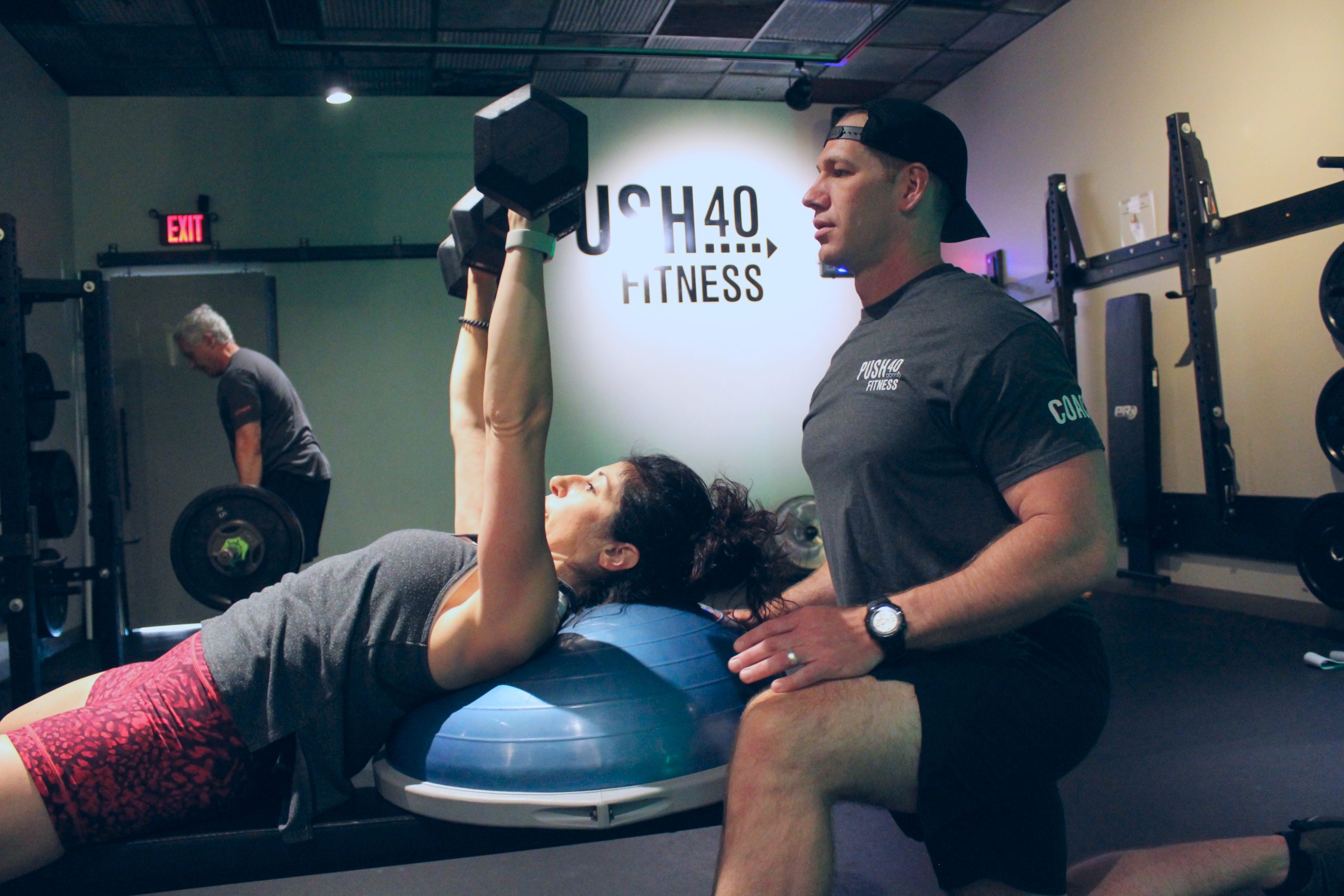 Coach Dan alongside a woman who is performing a dumbbell chest press.
