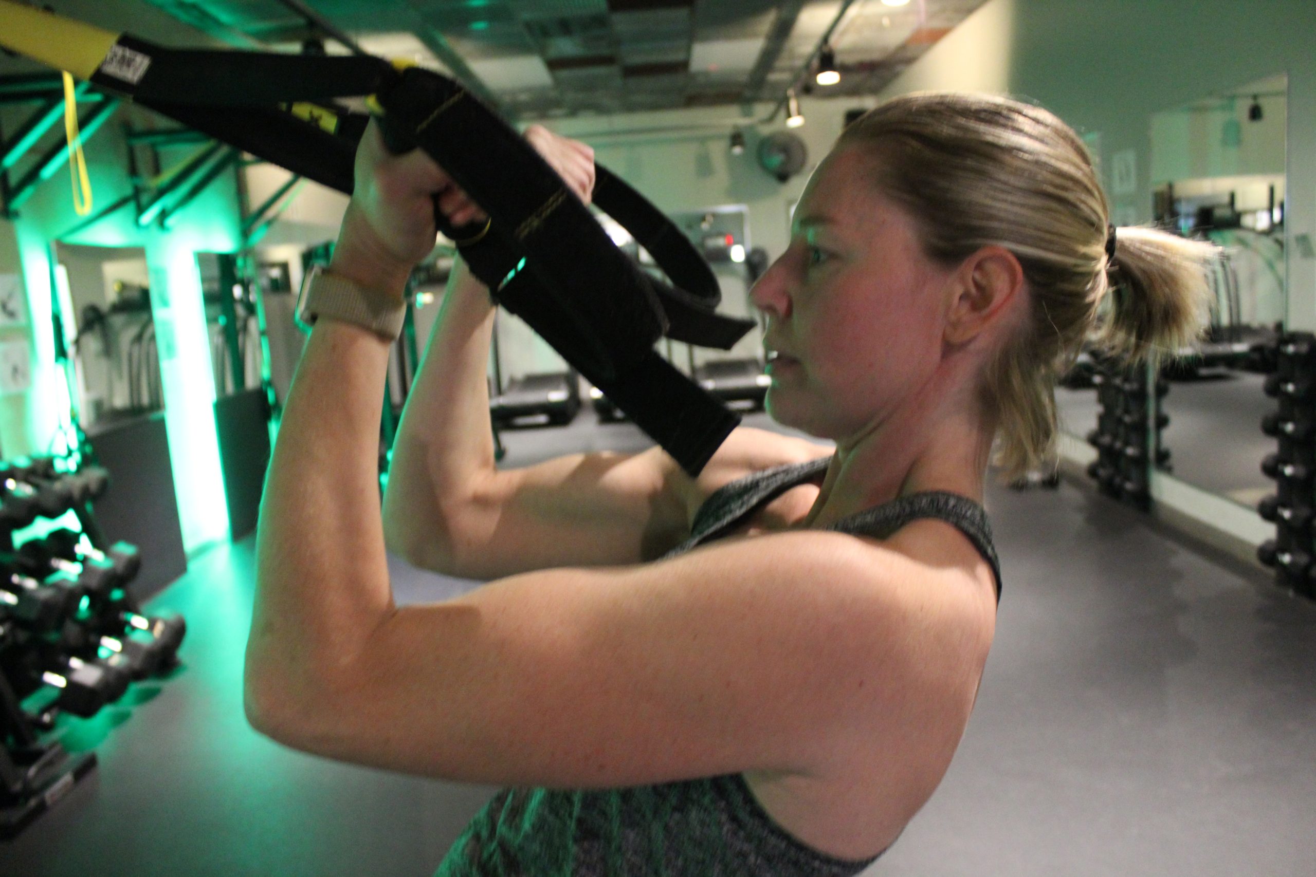 A woman doing bicep curls at the TRX station.